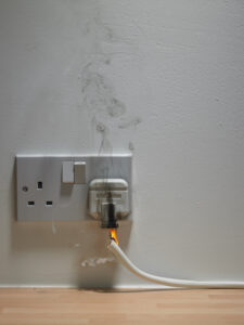 Electric plug in wall outlet with smoke and flame